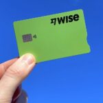 A hand holds a green Wise fintech credit card on a blue background