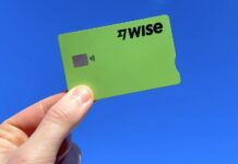 A hand holds a green Wise fintech credit card on a blue background