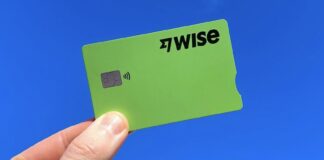 A hand holds a green Wise fintech credit card on a blue background