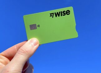 A hand holds a green Wise fintech credit card on a blue background