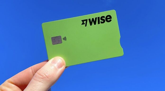 A hand holds a green Wise fintech credit card on a blue background