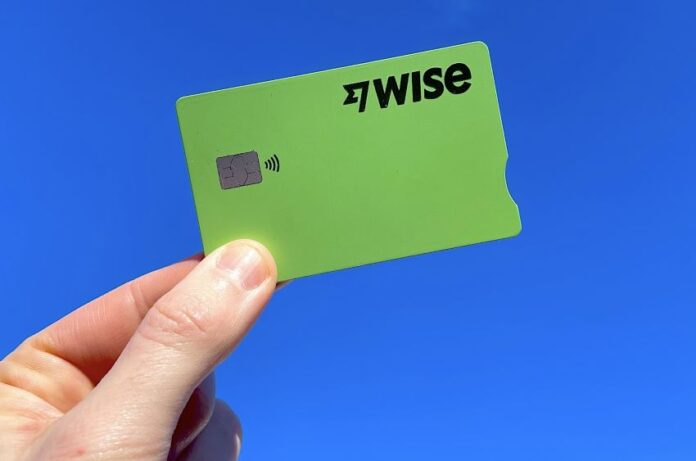 A hand holds a green Wise fintech credit card on a blue background