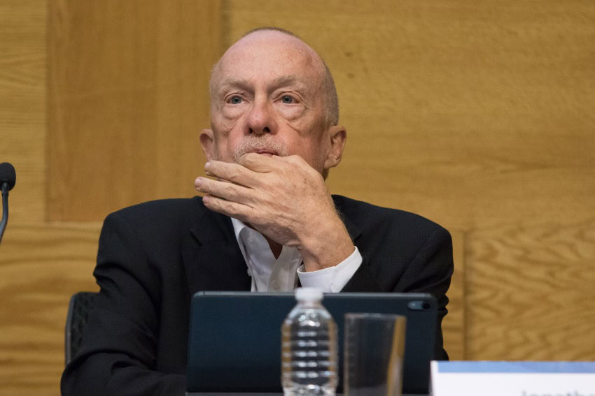 Jonathan Heath sitting at the bench of the board of governors of the Bank of Mexico. He is looking pensive, with his thumb and forefinger together on his chin.