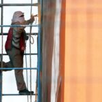 Man with his head and face covered with white cloths works on a building in Mexico City while standing on scaffolding next to the building.