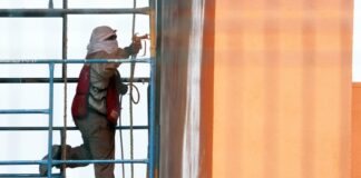Man with his head and face covered with white cloths works on a building in Mexico City while standing on scaffolding next to the building.