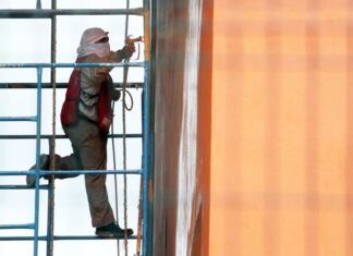 Man with his head and face covered with white cloths works on a building in Mexico City while standing on scaffolding next to the building.