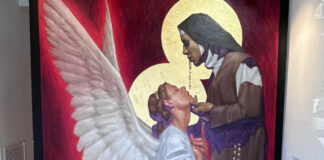 Painting of a nun in habit holding the chin of a kneeling angel all in white. They are painted against a blood-red background. The painting is titled "Anunciación" or Annunciation.