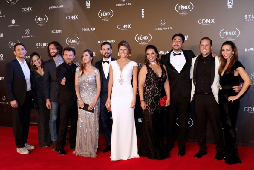 Cast of the TV show "Club de Cuervos" posing for paparazzi on a red carpet in front of a wall that has promotional wallpaper displaying the logos for Mexico's Fenix Awards, Mexico City InStyle magazine and others.