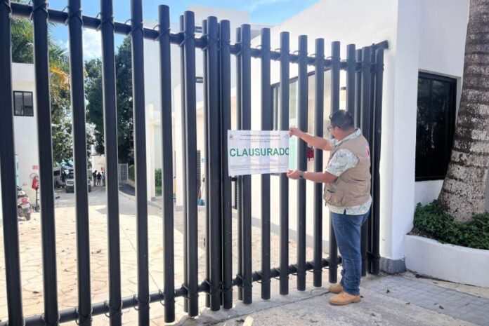 Man in a city government jacket putting a seal on a fenced gate to a hotel in Bacalar, Mexico. The seal says 