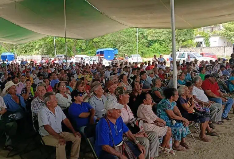 An audience of landowners sitting in folding chairs under an open-air tent in San Pedro Pochutla, Oaxaca.