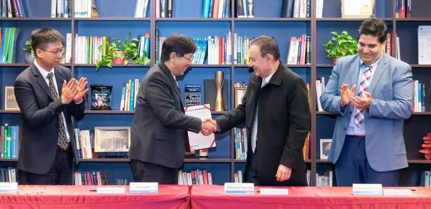 Sonora governor Alfonso Durazo shaking hands with Foxconn CEO Young Liu at a ceremony to sign a memorandum of understandingbetween the company and the state. Officials to the side of Durazo and Liu look on, applauding.