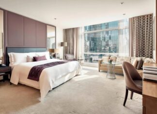 luxury hotel room in Mexico City with king sized bed in white with multiple pillows, a desk, sofa and coffee table and a view of a skyscraper across the street outside.