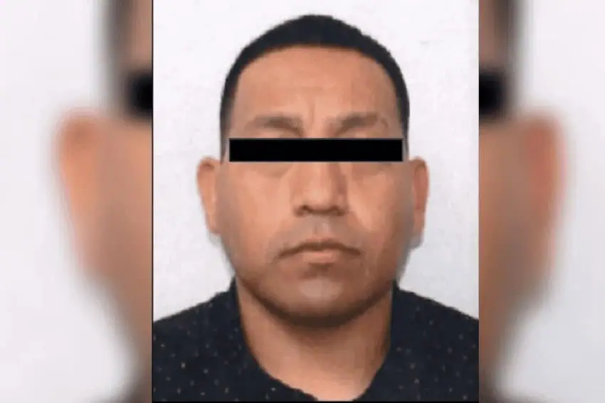 A mugshot of a middle-aged Mexican man. His eyes are redacted in the photo to prevent him from being identified. He has short dark hair and is wearing a black tee shirt.