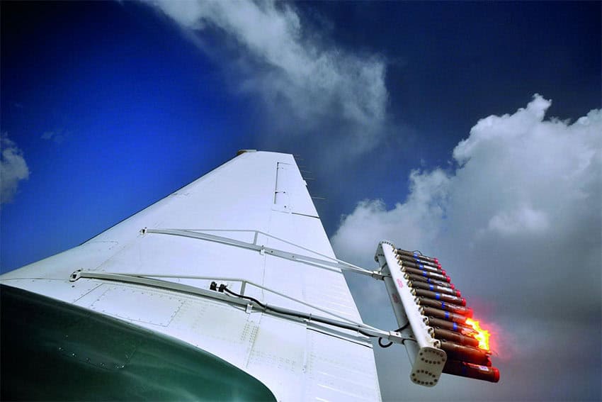 A device clipped to an airplane wing burns a substance to release it into the clouds