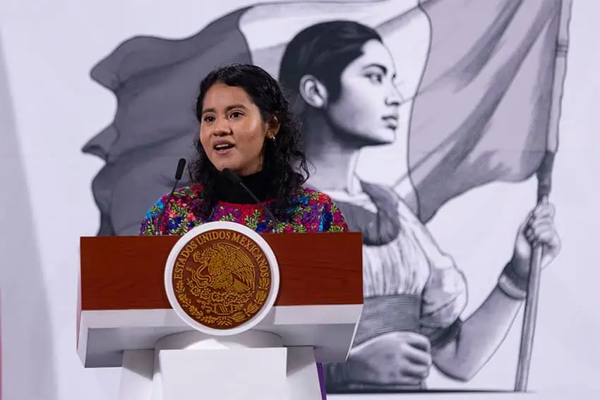 Nadia López García, a young morena woman wearing a huipil over a black long-sleeve shirt, stands at the National Palace podium