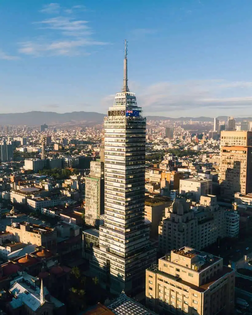 Mexico city skyline. At the center is a skyscraper with antennas at the top. In the background is a mountain range circling the city.