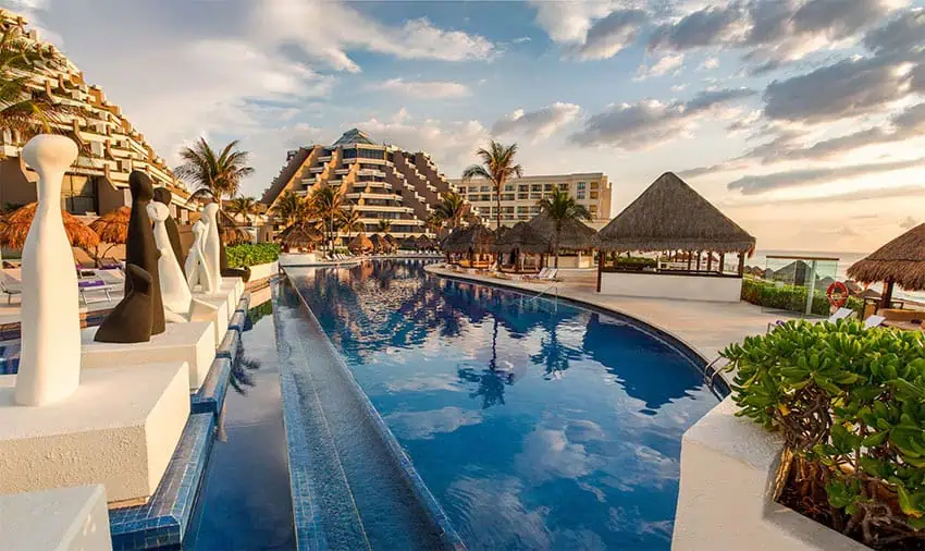 A large pool with palm trees and a pyramid-shaped hotel in the background