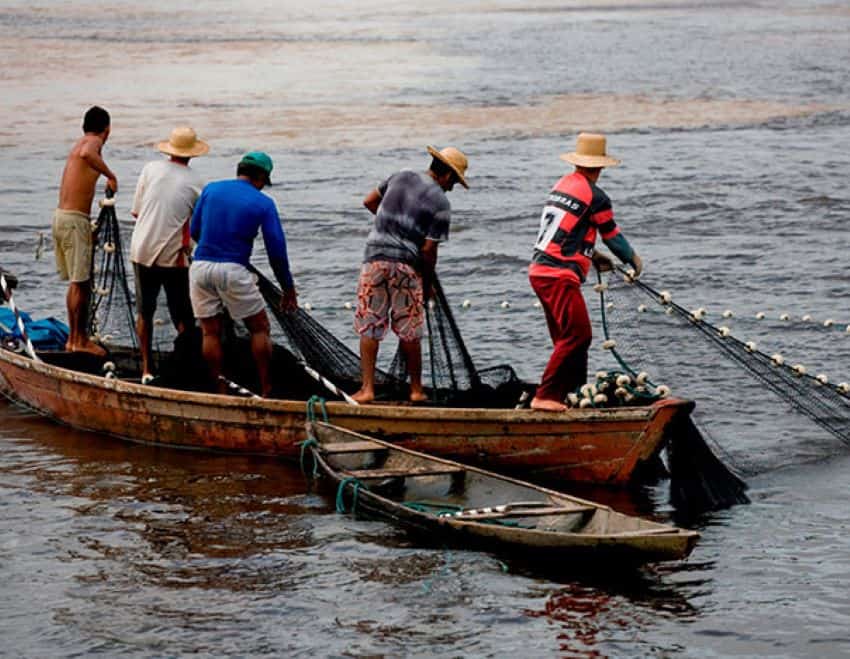 Five coastal fishermen on a row boat in Baja California Sur pulling in black nets in the water.