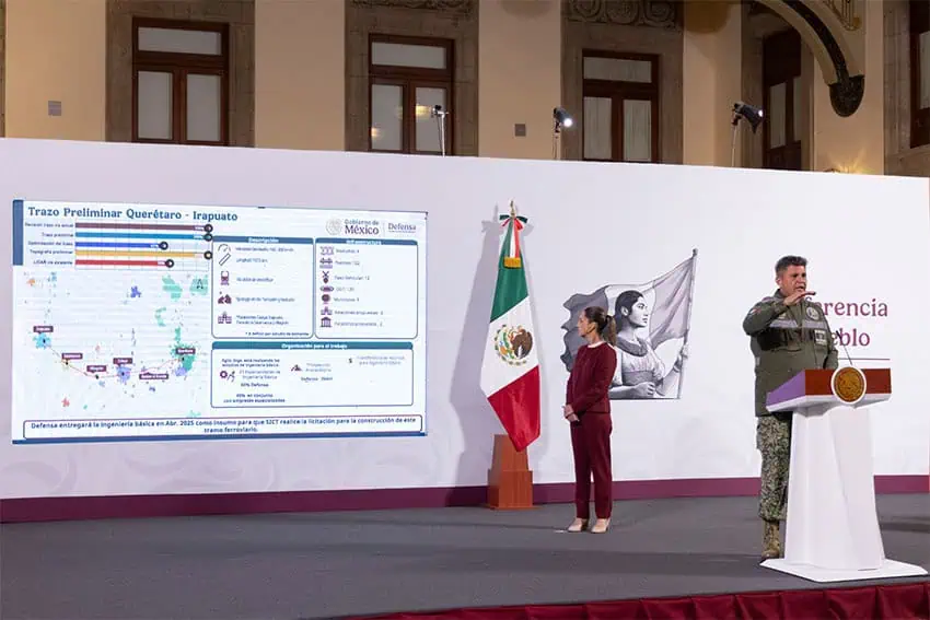 Jesús Antonio Esteva Medina, head of Mexico's transportation and highways agency, stands at Mexico's presidential podium during President Claudia Sheinbaum's daily press conference. He is holding his hand up near his face as if demonstrating a level or height as he speaks to reporters.