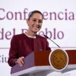 President Claudia Sheinbaum smiling as she stands at the presidential podium during a press conference discussing United States citizens arrested in Mexico