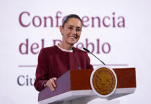 President Claudia Sheinbaum smiling as she stands at the presidential podium during a press conference discussing United States citizens arrested in Mexico