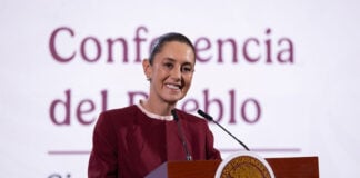 President Claudia Sheinbaum smiling as she stands at the presidential podium during a press conference discussing United States citizens arrested in Mexico