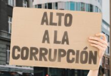 A hand holding up a sign saying in Spanish Alto a la Corrupcion (Stop the Corruption).