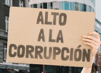 A hand holding up a sign saying in Spanish Alto a la Corrupcion (Stop the Corruption).