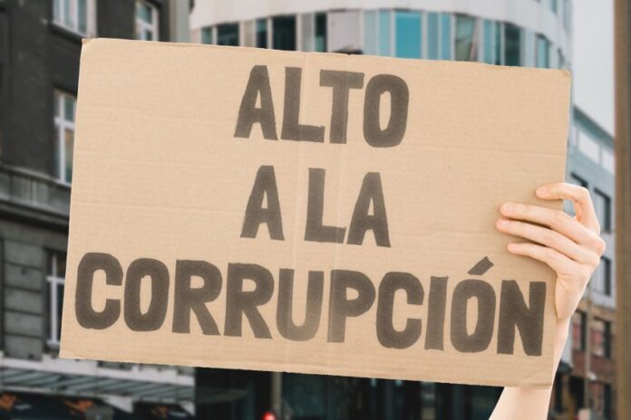 A hand holding up a sign saying in Spanish Alto a la Corrupcion (Stop the Corruption).