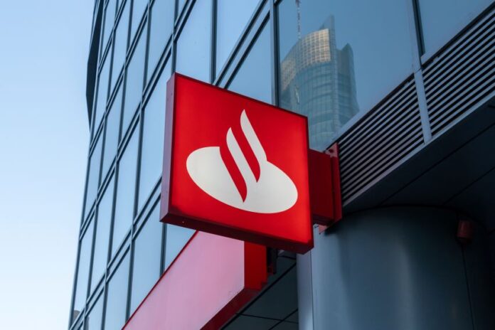 Sign with logo for Santander Bank, which has a red background and a stylized abstract image of a white swan. The sign is bolted toward the base of a skyscraper building.