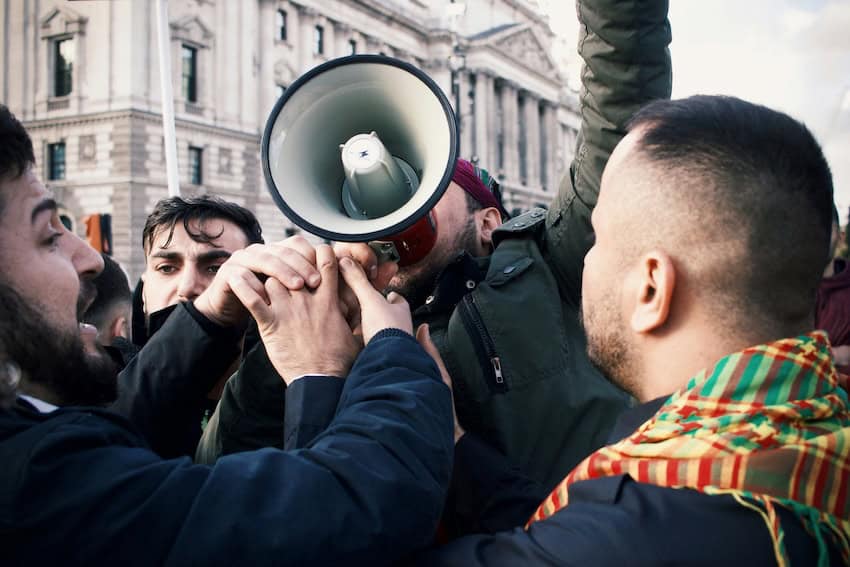 A man with a megaphone is mobbed by a crowd. Looks like a contentious expat relationship.