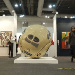 Spectators mill around an exhibition feature paintings and a large round sculpture at Zona Maco during Mexico City's Art Week 2025