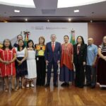 A group of Mexican politicians, administrators and academics stand in a group, several wearing clothing with traditional Indigenous designs