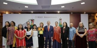 A group of Mexican politicians, administrators and academics stand in a group, several wearing clothing with traditional Indigenous designs