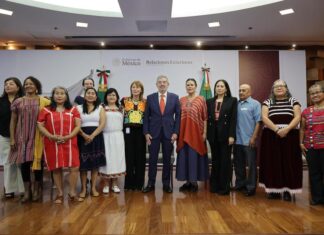 A group of Mexican politicians, administrators and academics stand in a group, several wearing clothing with traditional Indigenous designs