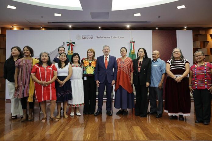 A group of Mexican politicians, administrators and academics stand in a group, several wearing clothing with traditional Indigenous designs