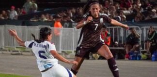 Two female soccer players wearing uniforms from different teams competing to take possession of the ball during a game
