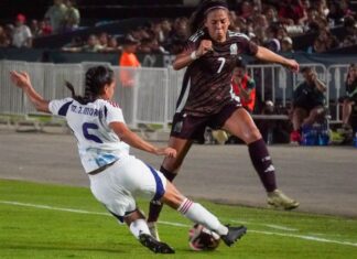 Two female soccer players wearing uniforms from different teams competing to take possession of the ball during a game