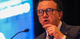 Coparmex business organization leader Juan José Sierra Álvarez standing at a podium with a microfone and pointing his finger emphatically as he speaks. He's in a suit and tie and wears black thick glasses.