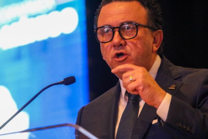 Coparmex business organization leader Juan José Sierra Álvarez standing at a podium with a microfone and pointing his finger emphatically as he speaks. He's in a suit and tie and wears black thick glasses.