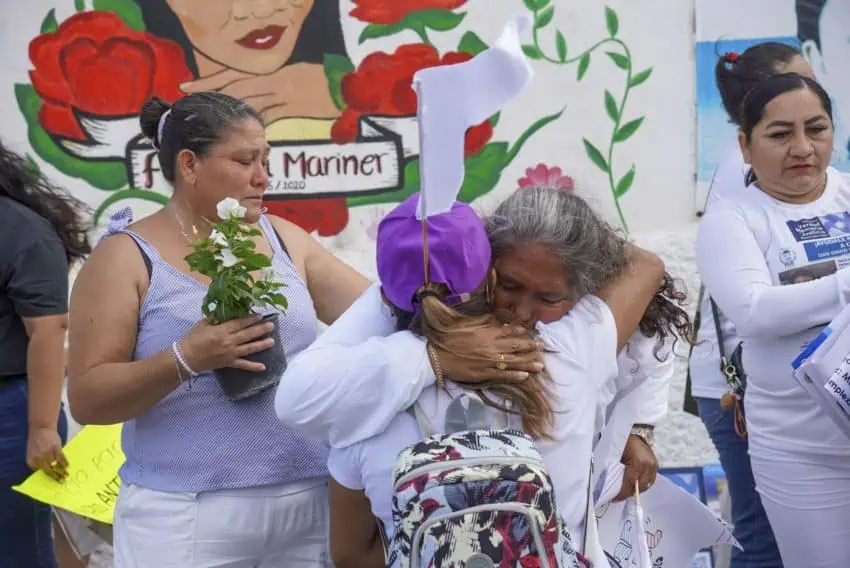 Middle aged Mexican women holding signs and papers behind the painting on a wall of a young Mexican woman.