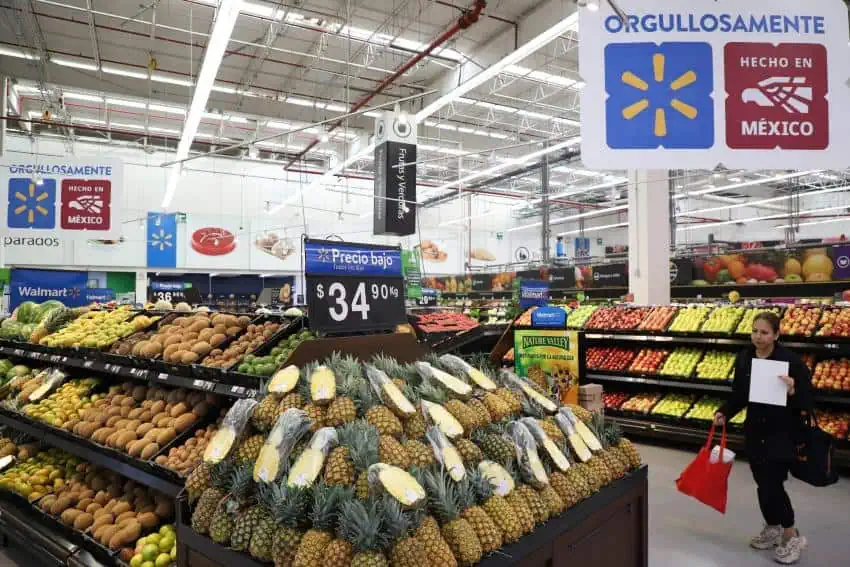 A Mexican woman walks through the produce section of Walmart in Mexico state. In the foreground is a display of pineapples for 34.90 pesos per kilo. In the aisles in the background are apples on display as well as mamey fruit.