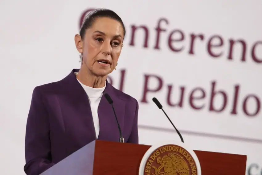 Claudia Sheinbaum at the presidential podium looking stern as she talks to reporters off camera.