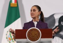 President Claudia Sheinbaum standing at the presidential podium during her daily press conference, speaking about tariffs on Mexican exports.