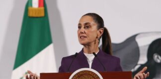 President Claudia Sheinbaum standing at the presidential podium during her daily press conference, speaking about tariffs on Mexican exports.