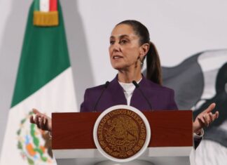 President Claudia Sheinbaum standing at the presidential podium during her daily press conference, speaking about tariffs on Mexican exports.