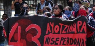 Protesters hold a large banner reading "43 Ayotzinapa, no se perdona, no se olvida"