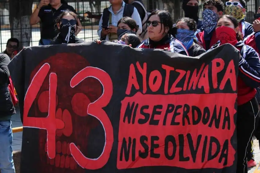 Mexicans at a vigil holding up a banner with the words "43" and Ayotzinapa and in Spanish "Never forgive, never forget."