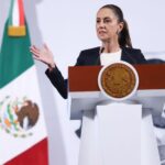 President Claudia Sheinbaum of Mexico standing at the presidential podium during her daily press conference. She is talking to reporters with her hands stretched out on either side of her body.