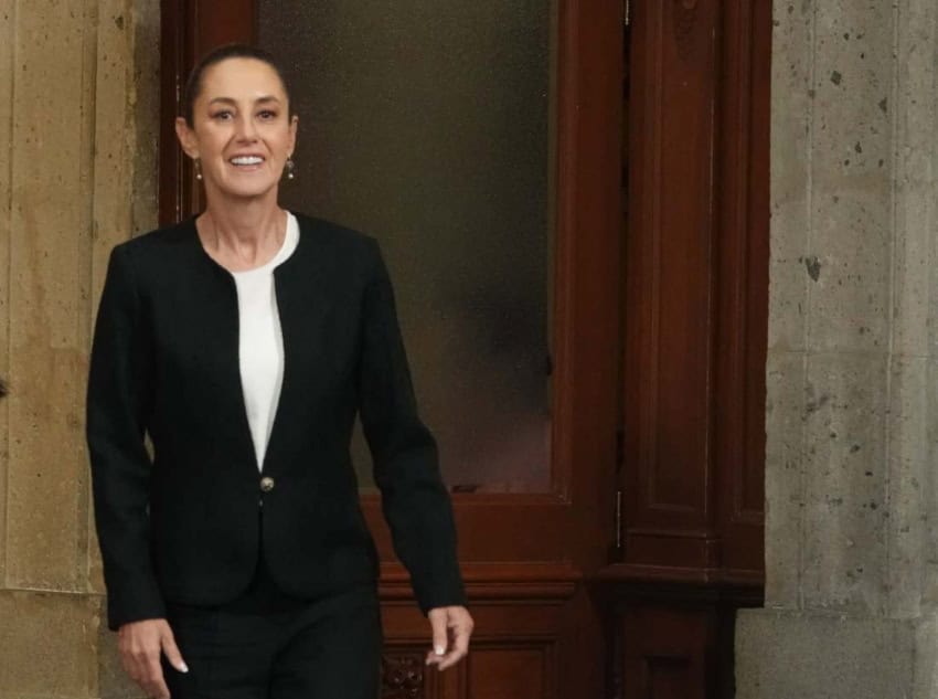 Claudia Sheinbaum entrando en la sala de información de la prensa en el Palacio Nacional de México. Ella está sonriendo mientras camina hacia la cámara.